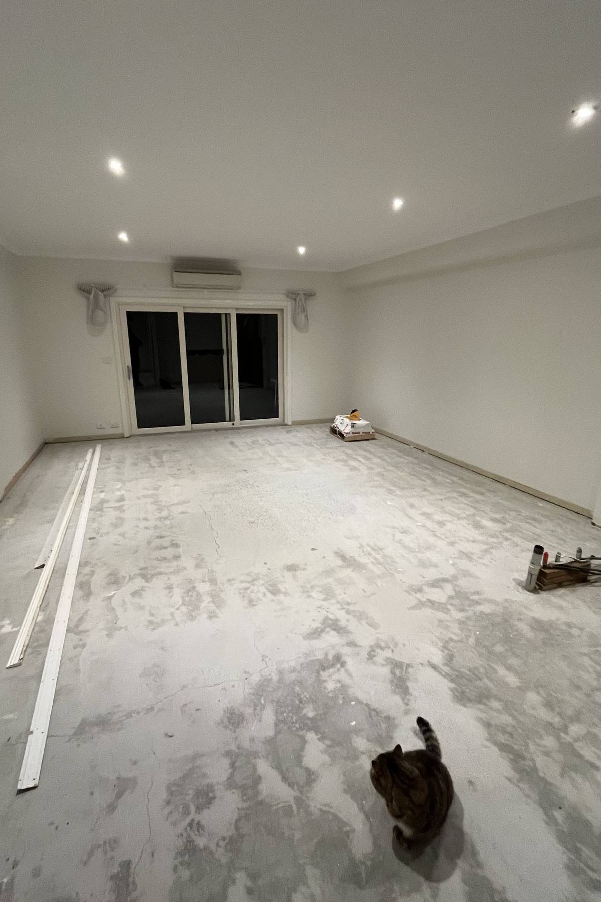 Empty living and dining area with a bare slab floor and a sliding door to a courtyard.