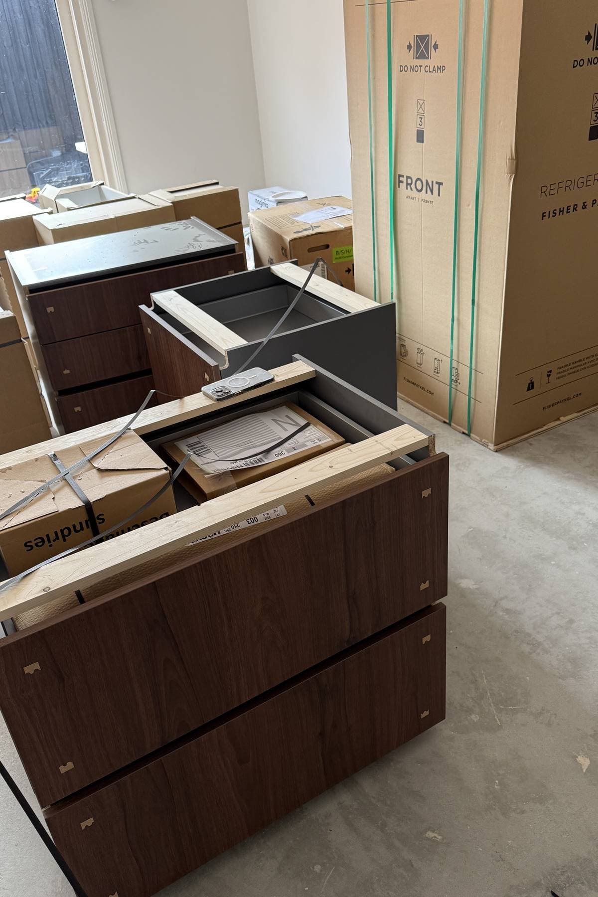 Walnut drawer units unwrapped on the floor beside boxed appliances.