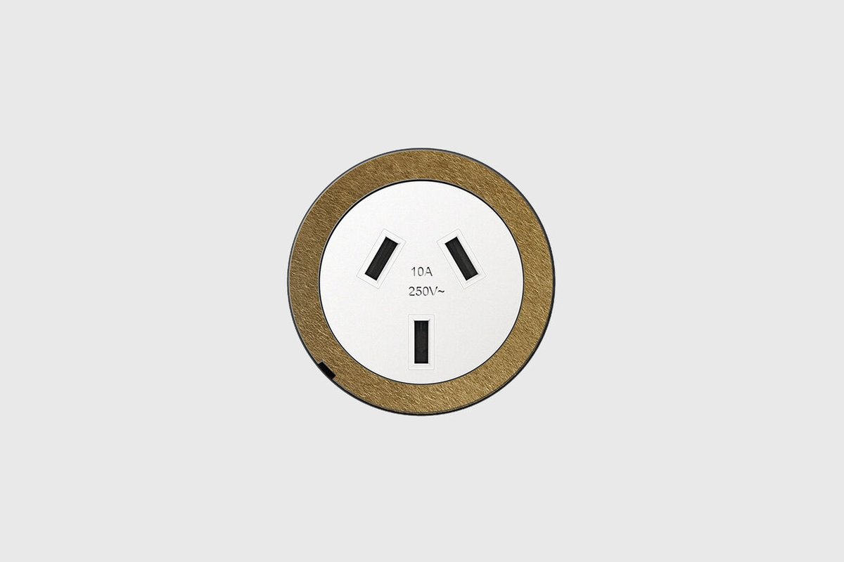 Round flush power outlet with a white face and a brushed brass surround.