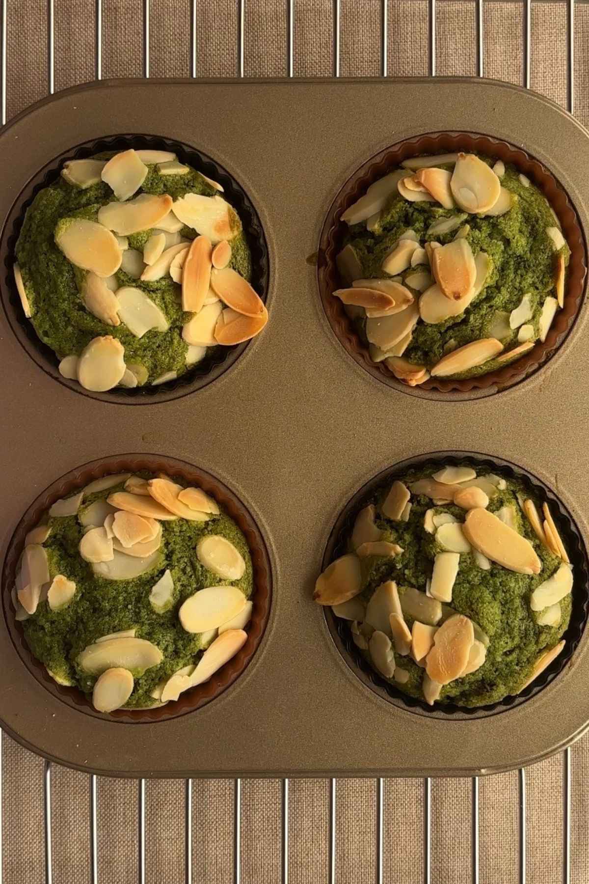 Overhead shot of four freshly baked matcha muffins in a cooling rack.