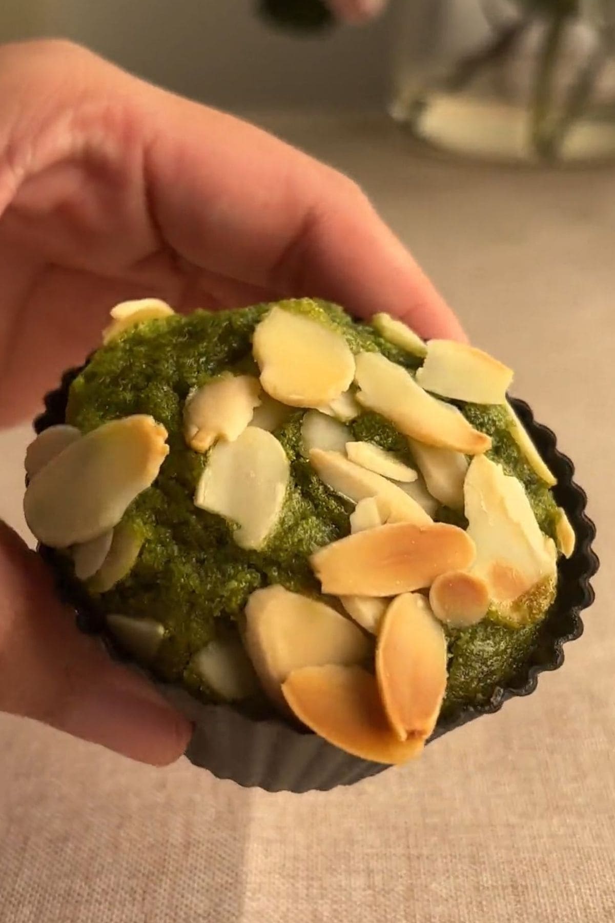 Hand holding a matcha muffin with toasted sliced almond toppings.