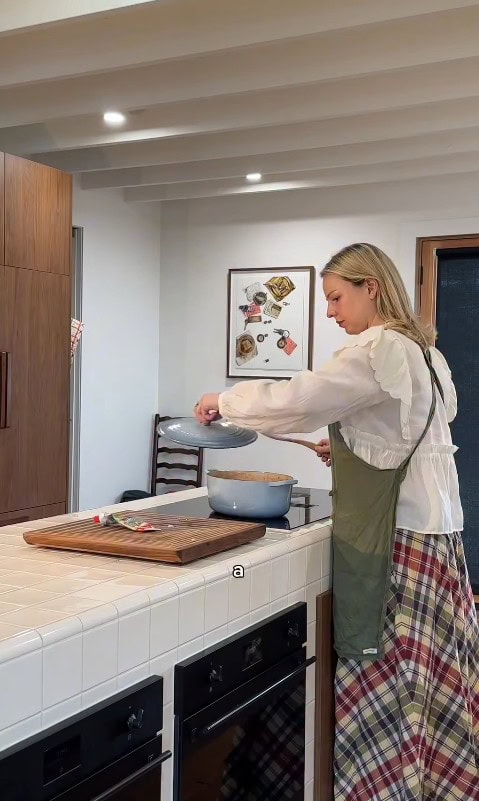 Woman cooking in kitchen with tiled white bench.