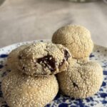 A stack of sesame-coated cookies, the top one split open showing chocolate chunks.