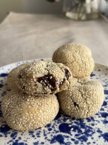 A stack of sesame-coated cookies, the top one split open showing chocolate chunks.