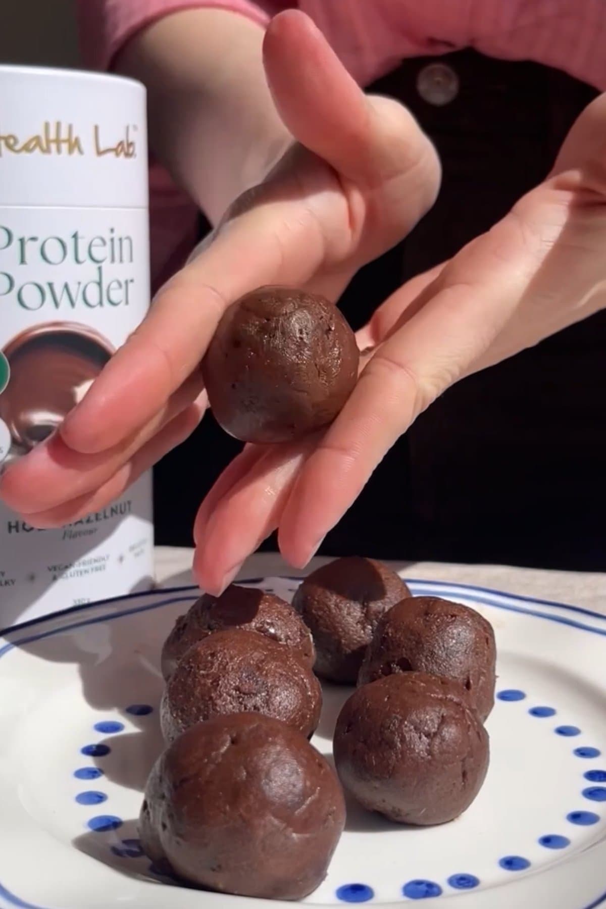 A hand holding a rolled chocolate protein ball.