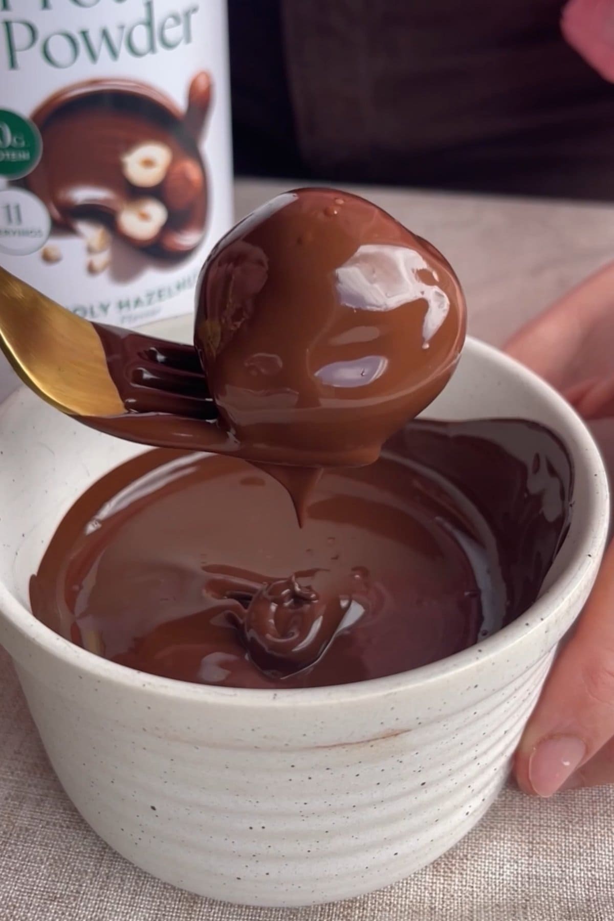 A protein ball dipped in melted chocolate and lifted on a fork.