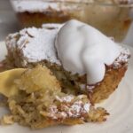 Gold fork cutting into a baked oat square with powdered sugar, flaked almonds and a creamy topping.